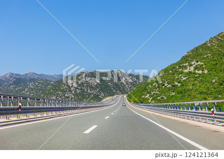 Open road leads between green mountains under bright sky. This sunny highway in Croatia captures freedom and scenic drive across a lush Mediterranean landscape, inviting endless exploration 124121364