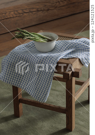 Fresh asparagus in ceramic bowl on rattan stool with linen tea towel. Healthy lifestyle concept 124121525