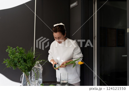 Woman arranging yellow tulip and greenery at a modern workspace during daylight 124121550