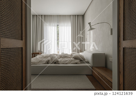wabi-sabi bedroom features an oak bedside table, textured clay wall decor, soft linen bed linens, a neutral grey rug, and a woven rattan wardrobe, creating a harmonious blend of natural materials and 124121639