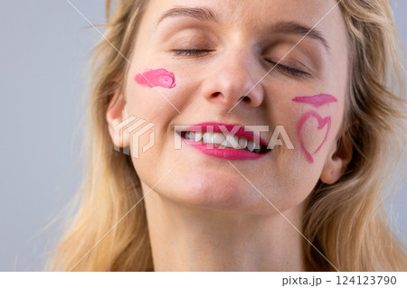 A joyful woman with playful pink makeup expressions on her face, symbolizing love and happiness, captured against a light gray background, radiating positivity and cheerfulness. A joyful woman with playful pink makeup expressions on her face, symbolizing love and happiness, captured against a light gray background, radiating positivity and cheerfulness. 124123790