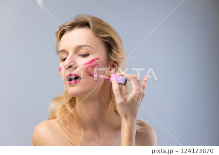 A Playful Exploration of Beauty: Woman Applying Pink Makeup with Heart and Line Designs on Her Face, Evoking Fun and Creativity in Personal Expression. 124123870