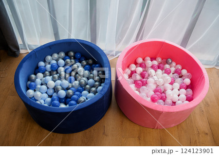 Two Colorful Children's Ball Pits Filled with Blue, White, Gray and Pink, White Play Balls on Wooden Floor Next to Curtain Two Colorful Children's Ball Pits Filled with Blue, White, Gray and Pink, White Play Balls on Wooden Floor Next to Curtain 124123901