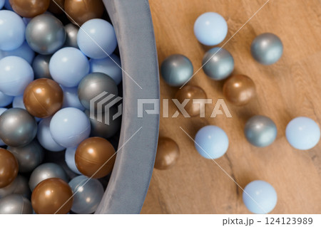 Multicolored Plastic Balls Scattered Around and Inside Soft Play Pit on Wooden Floor from Above 124123989