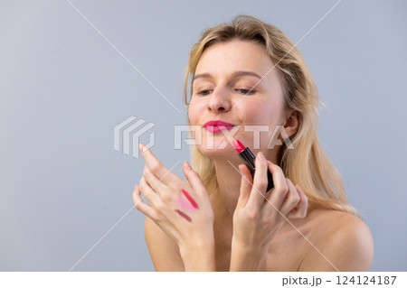 Woman Applying Lipstick with Soft Expression, Showcasing Rich Colors on Her Hand and Bright Lips, Perfect for Fashion and Makeup Enthusiasts Seeking Inspiration 124124187