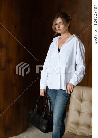 A girl in a white shirt and blue jeans is posing with a black bag. A girl in a white shirt and blue jeans is posing with a black bag. 124125487