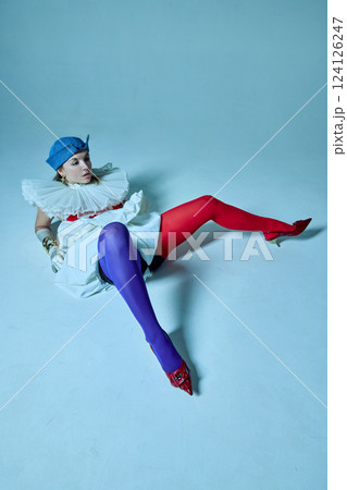 Woman in striking red and blue tights lies on floor with legs wide apart, against studio background. View from above. 124126247