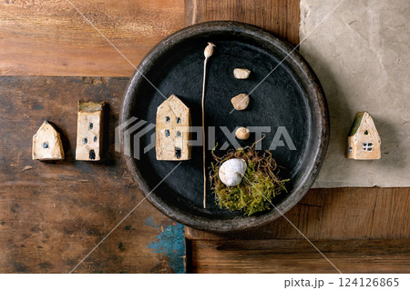 Close up black ceramic bowl with miniature ceramic house, small pebbles, moss nest with shell on rustic wooden background. Natural materials artistic composition with contrast textures. home concept Close up black ceramic bowl with miniature ceramic house, small pebbles, moss nest with shell on rustic wooden background. Natural materials artistic composition with contrast textures. home concept 124126865