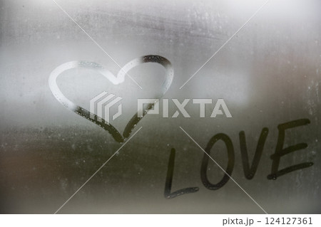 Beautiful heart symbol and love word on the glass window with water drobs.  124127361