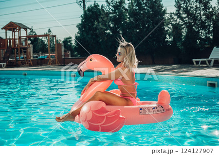 A woman is sitting on a pink flamingo float in a pool. The scene is bright and cheerful, with the woman enjoying her time in the water. A woman is sitting on a pink flamingo float in a pool. The scene is bright and cheerful, with the woman enjoying her time in the water. 124127907