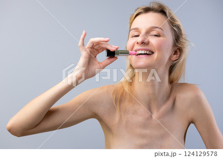 A Bright Smile: Capturing Joy and Beauty in a Playful Makeup Moment Featuring a Woman Holding Pink Lipstick 124129578