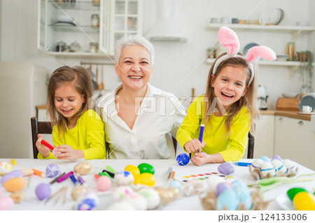 Happy Easter. Two little girls sisters twins grandmother painting eggs enjoying time together. Happy family grandma granddaughters child kids preparing for Easter. Spring Christian festival tradition Happy Easter. Two little girls sisters twins grandmother painting eggs enjoying time together. Happy family grandma granddaughters child kids preparing for Easter. Spring Christian festival tradition 124133006