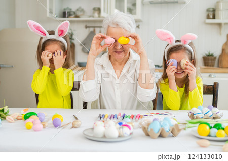 Happy Easter. Two little girls sisters twins grandmother painting eggs enjoying time together. Happy family grandma granddaughters child kids preparing for Easter. Spring Christian festival tradition Happy Easter. Two little girls sisters twins grandmother painting eggs enjoying time together. Happy family grandma granddaughters child kids preparing for Easter. Spring Christian festival tradition 124133010