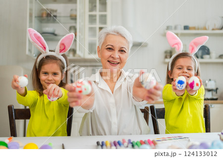 Happy Easter. Two little girls sisters twins grandmother painting eggs enjoying time together. Happy family grandma granddaughters child kids preparing for Easter. Spring Christian festival tradition Happy Easter. Two little girls sisters twins grandmother painting eggs enjoying time together. Happy family grandma granddaughters child kids preparing for Easter. Spring Christian festival tradition 124133012