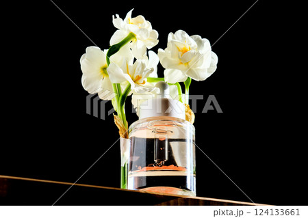 Serum bottle with petals on black background with daffodils. 124133661