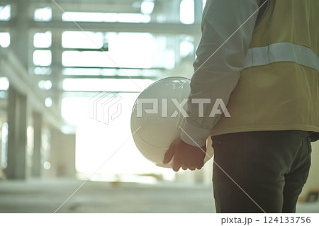Construction engineer holding hardhat inspecting building site during bright day 124133756