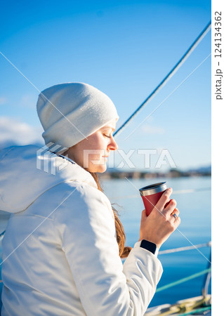 Woman hands holding thermo mug sitting on bow of the yacht during sailing in the morning in winter time in Adriatic sea, relaxation in yachting time Woman hands holding thermo mug sitting on bow of the yacht during sailing in the morning in winter time in Adriatic sea, relaxation in yachting time 124134362