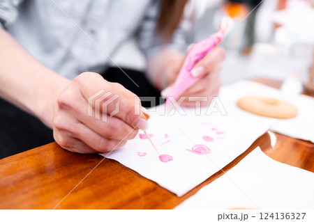 Young caucasian female decorating cookies with pink frosting in a bakery setting Young caucasian female decorating cookies with pink frosting in a bakery setting 124136327