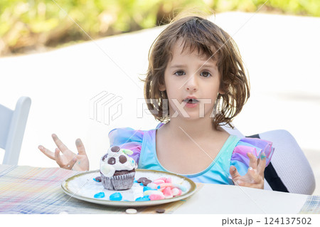 Daycare activity, toddler girl is decorating a cupcake outdoors. Daycare activity, toddler girl is decorating a cupcake outdoors. 124137502