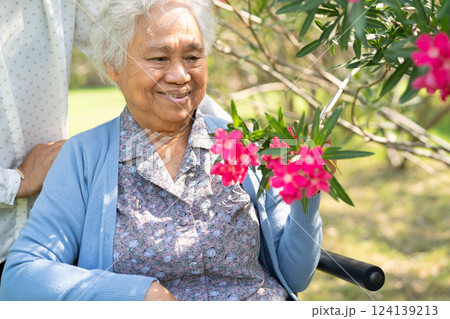 Asian elderly woman holding red rose flower, smile and happy in the sunny garden. 124139213