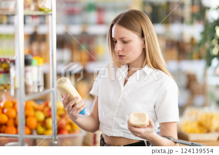 Choose food in supermarket - woman chooses mayonnaise to buy in the grocery department section of store 124139554