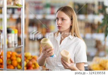 Young woman choosing mayonnaise in grocery store Young woman choosing mayonnaise in grocery store 124139558