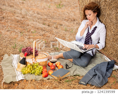 Woman in office clothes on picnic working on laptop while sitting near hay bales outdoor 124139599