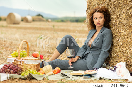 Woman in unbuttoned jacket with bare chest sits near hay bale on picnic Woman in unbuttoned jacket with bare chest sits near hay bale on picnic 124139607