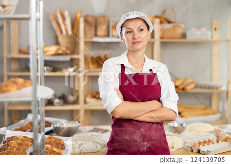 Confident young female bakery in apron posing with arms crossed indoors in bakery kitchen 124139705