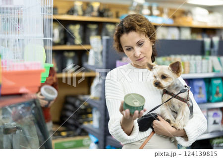Buyers woman with Yorkshire Terrier choose healthy food and nutrition for pet in tin can 124139815