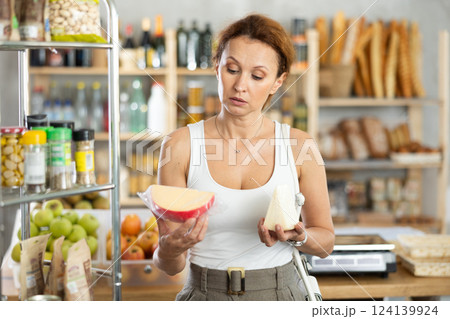 Woman carefully chooses delicious cheese in grocery department of supermarket 124139924