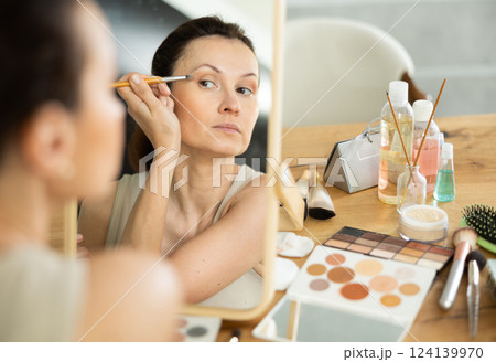 Woman applying eyeshadow with brush during daily makeup 124139970