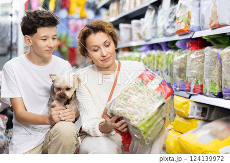 Woman with teenage son and Yorkshire terrier choosing straw bedding in pets store 124139972