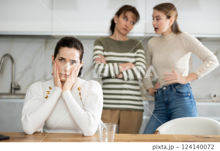 Upset middle-aged woman sitting at the kitchen table with her back to women quarreling to her 124140072