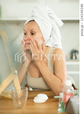 Middle-aged woman examining her facial skin looking in the mirror put on the table 124140186