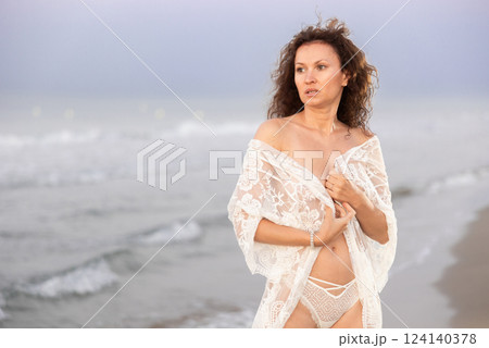 Woman in white negligee stands on coast Woman in white negligee stands on coast 124140378