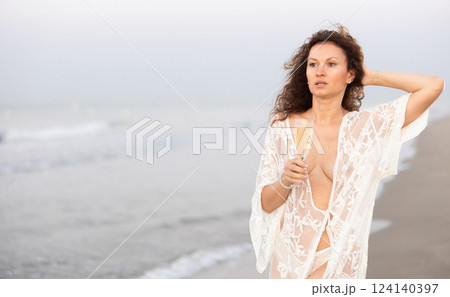 Woman in white negligee with champagne on coast Woman in white negligee with champagne on coast 124140397