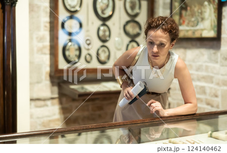 Woman with paper and phone in hands walks around hall of museum, examines showpiece at exhibition Woman with paper and phone in hands walks around hall of museum, examines showpiece at exhibition 124140462