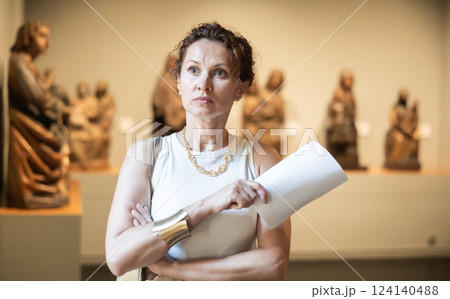 Interested young woman looking at collection of medieval sculptures and objects in museum 124140488