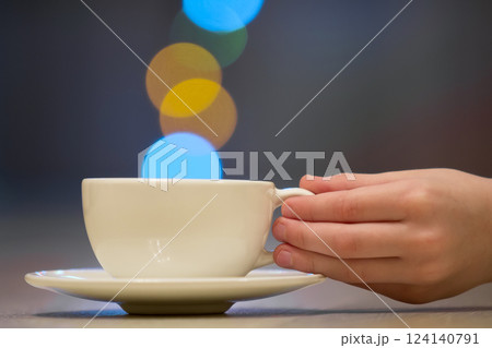 Hand holding white cup of coffee with colorful bokeh steam Hand holding white cup of coffee with colorful bokeh steam 124140791