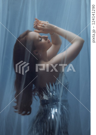 Dreamy Portrait of a Woman in a Silver Dress Behind Sheer Fabric 124141290