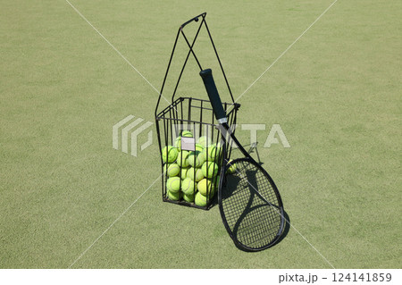 Tennis racket with a basket of balls, on a green background. Tennis racket with a basket of balls, on a green background. 124141859
