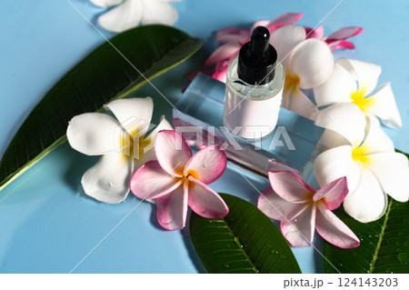 Serum bottle rests amidst fresh plumeria blossoms, enhancing a serene spa atmosphere with hydration. 124143203