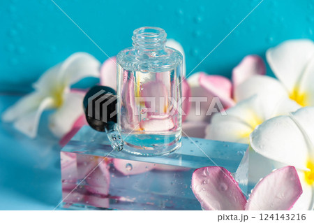 A glistening serum in a dropper bottle sits on a clear block with fresh flowers nearby. A glistening serum in a dropper bottle sits on a clear block with fresh flowers nearby. 124143216