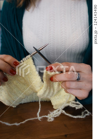 Women hands holding knitting needles and yellow cotton knitted work. Knitting woman with bobbins of yarn and yellow knitwear. Needlework in process. Knitting hobby. Knitter work.  124143490