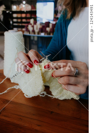 Women hands holding knitting needles and yellow cotton knitted work. Knitting woman with bobbins of yarn and yellow knitwear. Needlework in process. Knitting hobby. Knitter work.  124143491