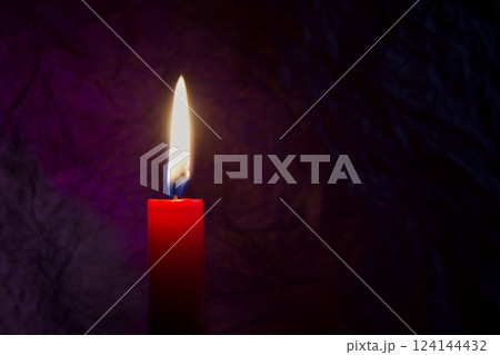 Red candle with flickering flame against a textured dark background 124144432