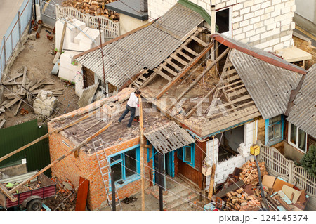 An old, dilapidated house with a worn-out wooden roof, showing signs of renovation. The exterior of the building is in ruins, with traces of war damage 124145374