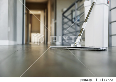 Cleaning supplies: mop and bucket with wringer sitting on wooden laminate floor in modern corridor, wet equipment tools, housekeeping concept. Emphasizing home sanitation, cleanliness, hygiene Cleaning supplies: mop and bucket with wringer sitting on wooden laminate floor in modern corridor, wet equipment tools, housekeeping concept. Emphasizing home sanitation, cleanliness, hygiene 124145728
