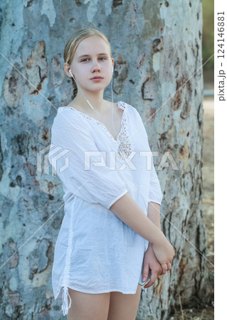 Teenage girl in headphones standing on the background of tree Teenage girl in headphones standing on the background of tree 124146881